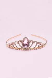 Gold tiara with pink gemstone on pink background.