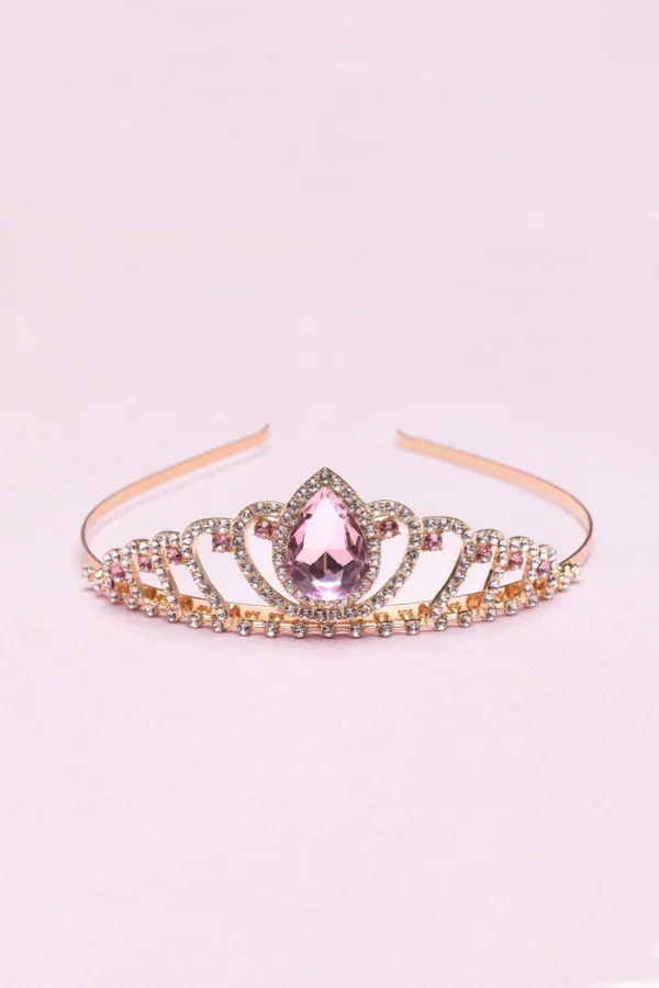 Gold tiara with pink gemstone on pink background.