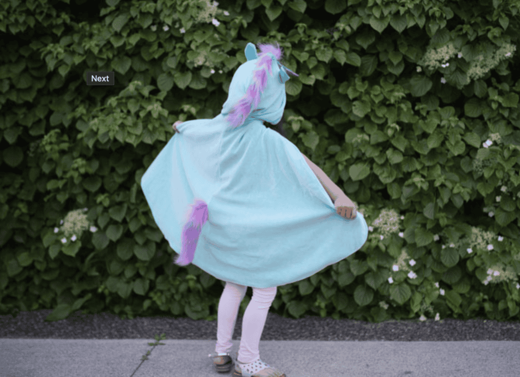 Child in unicorn costume near green bushes.
