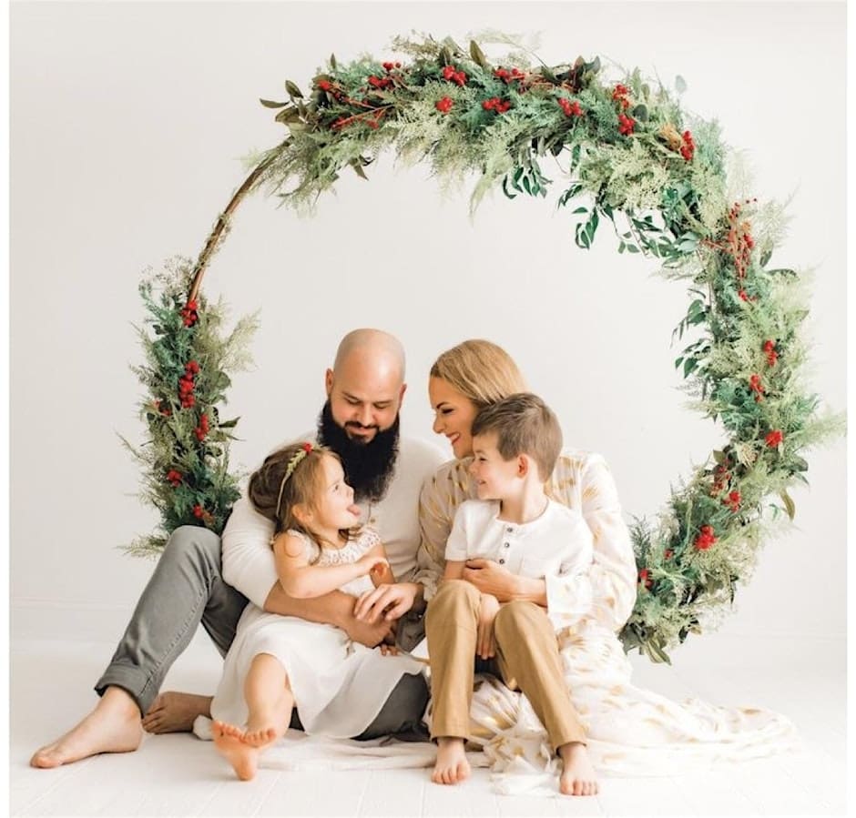 Family sitting under festive greenery wreath.