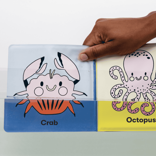 Hand holding animal-themed children's book in water.