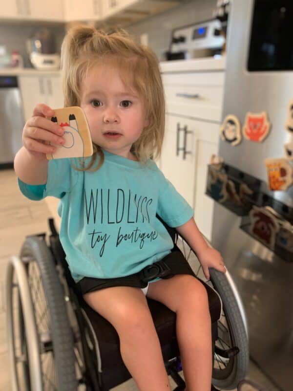 Child in wheelchair holding toy by fridge
