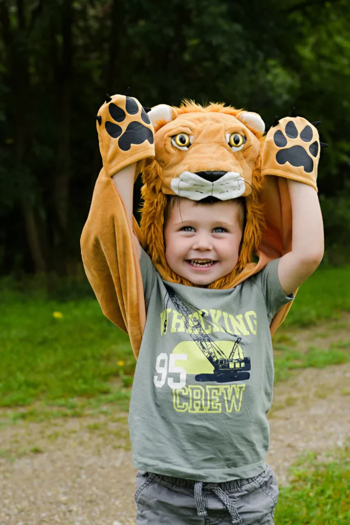 Child wearing lion costume, smiling outdoors.