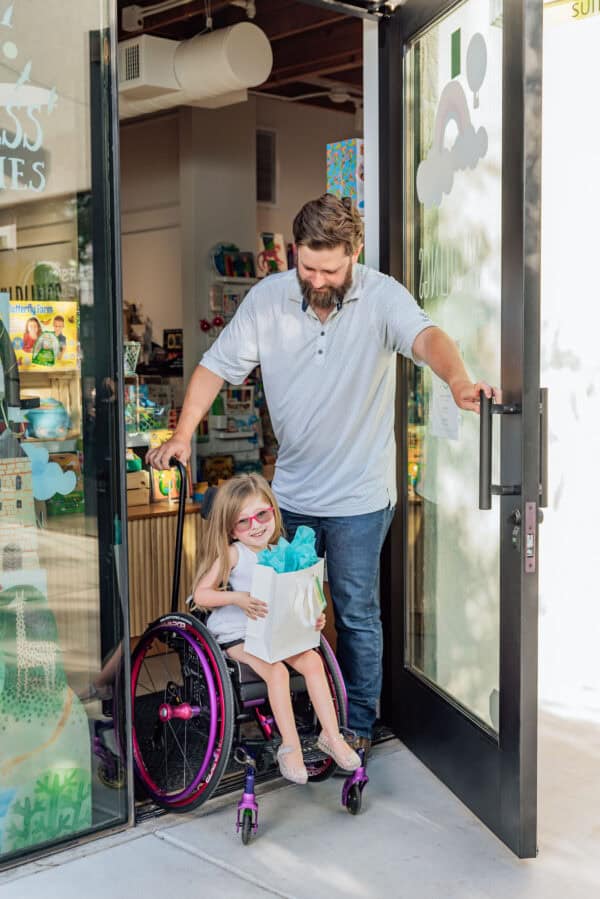 Man assisting girl in wheelchair through door