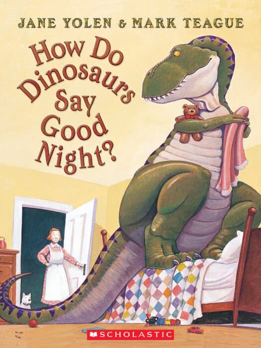 Dinosaur sitting on bed with teddy and blanket.