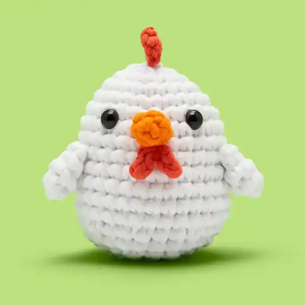 Crocheted chicken toy with orange beak, green background.
