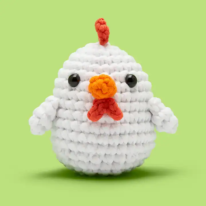 Crocheted chicken toy with orange beak, green background.