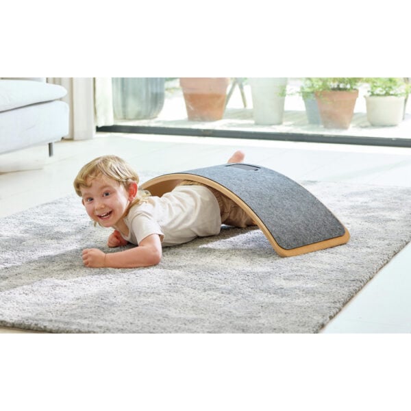 Child playing under curved gray board indoors.