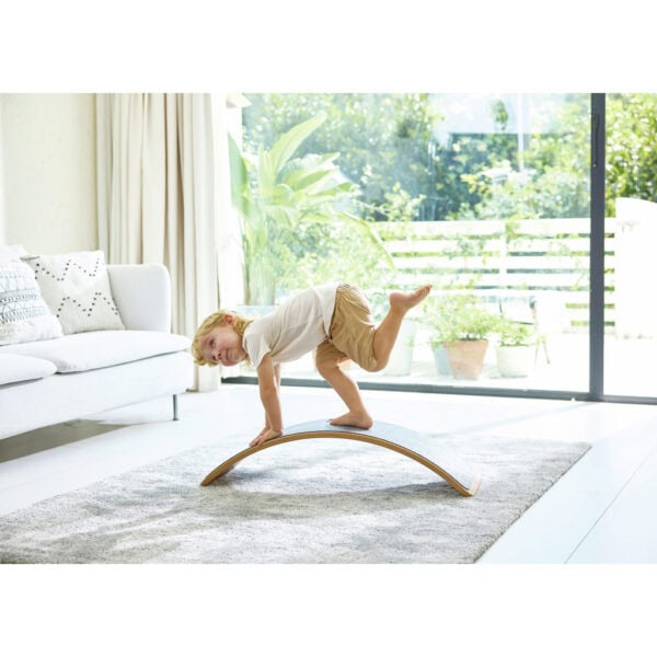 Child balancing on curved board in living room.