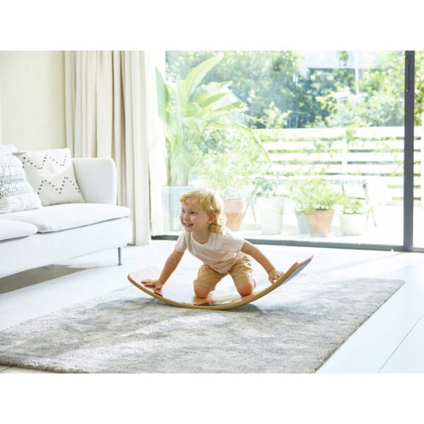 Child playing on wooden balance board indoors.