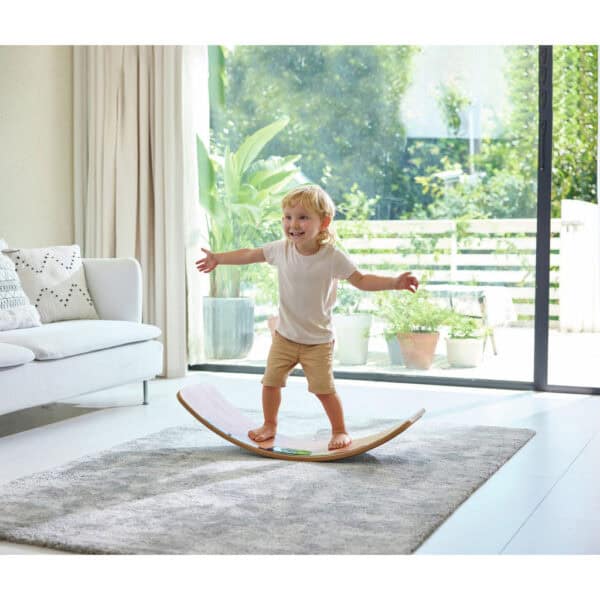 Child balancing on wooden board in living room.