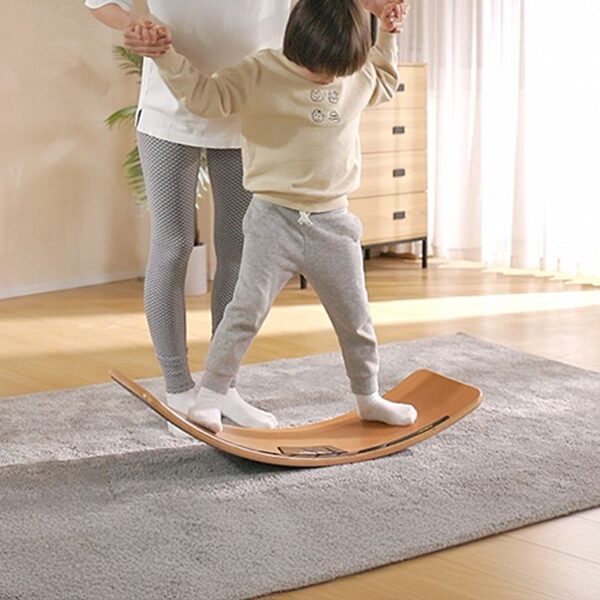 Child balancing on a wooden balance board indoors.