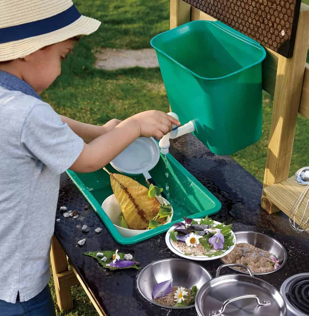 Child playing in outdoor mud kitchen with water.