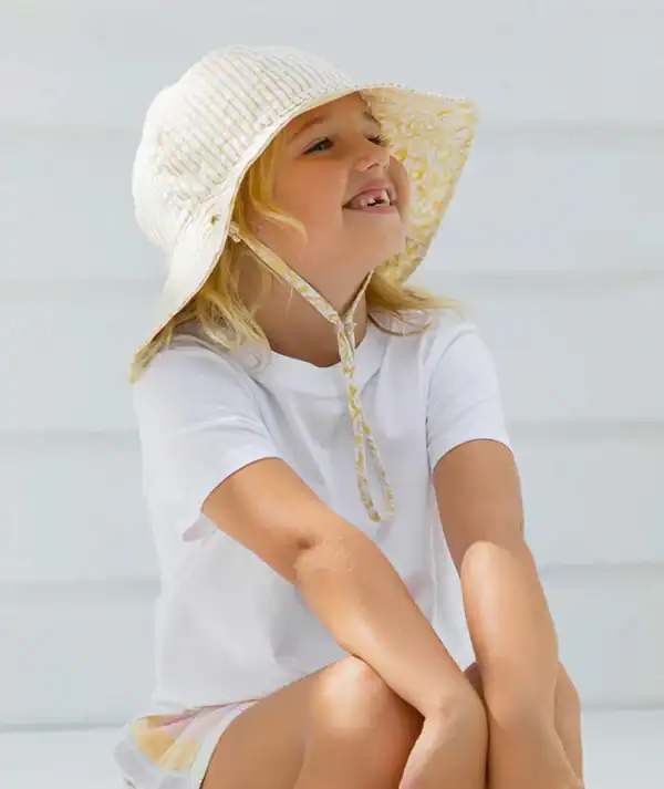 Smiling child in sun hat sitting happily.