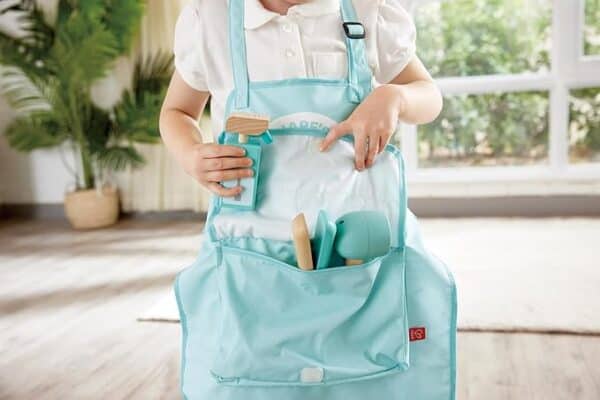 Child wearing gardening apron with tools inside pockets.