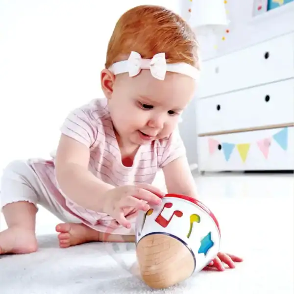 Baby playing with colorful wooden toy on floor.