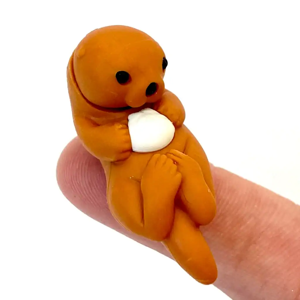 Clay otter figure holding white object on finger