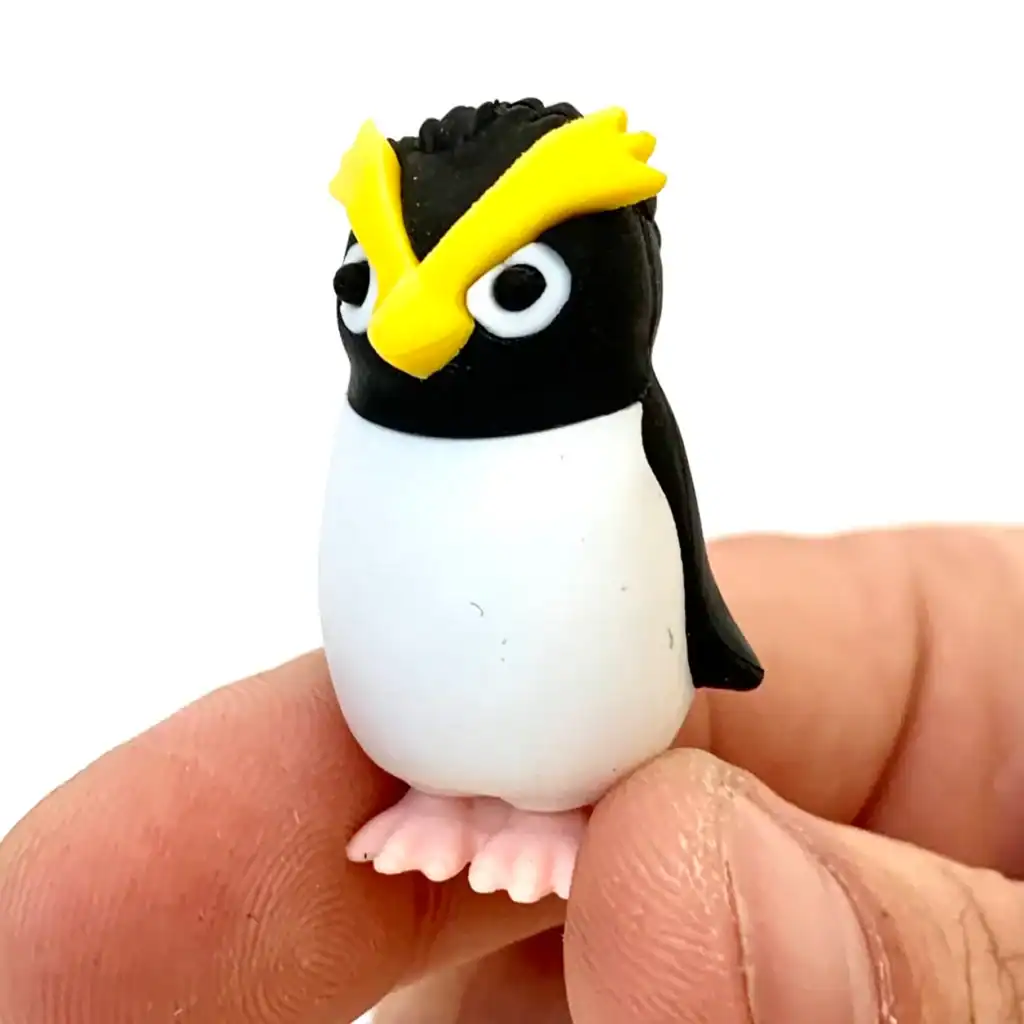Hand holding a small penguin figurine with eyebrows.