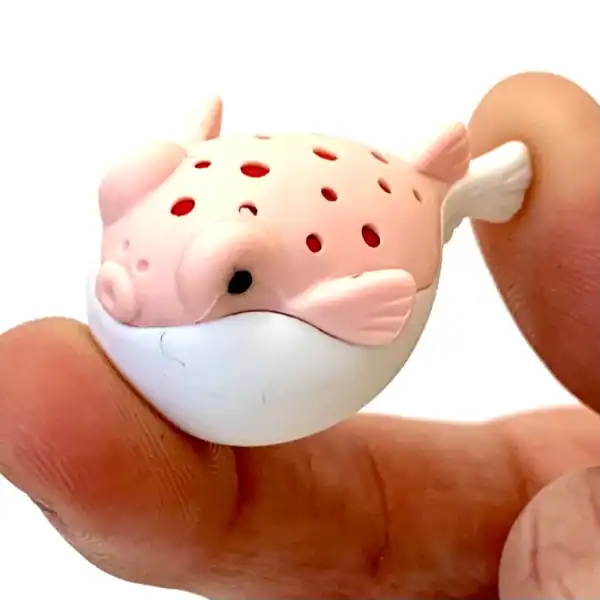 Small pink pufferfish figurine held between fingers.