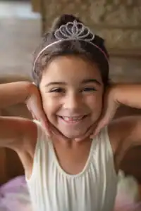 Smiling child wearing a tiara indoors.