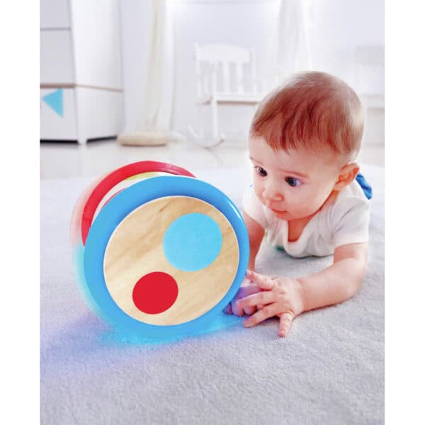 Baby crawls toward colorful rolling toy indoors.