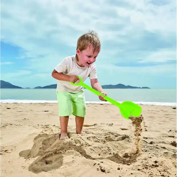 Child playing with shovel on sandy beach.