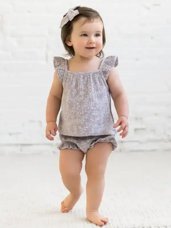Smiling toddler in grey outfit with a bow.
