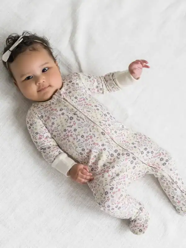 Baby in floral onesie lying on white blanket.