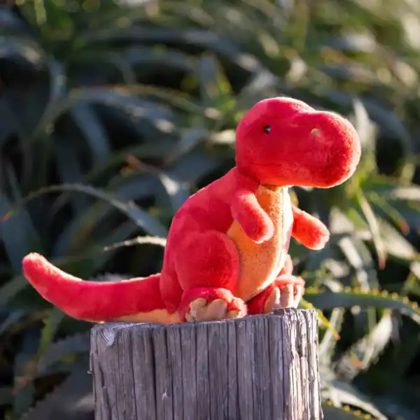 Red plush dinosaur on tree stump outdoors.