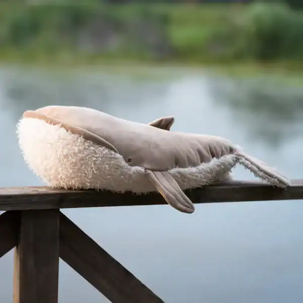 Plush whale toy on wooden railing by lake.