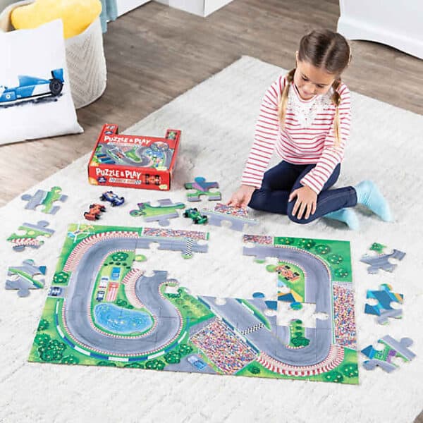 Child assembling a race track puzzle on floor.