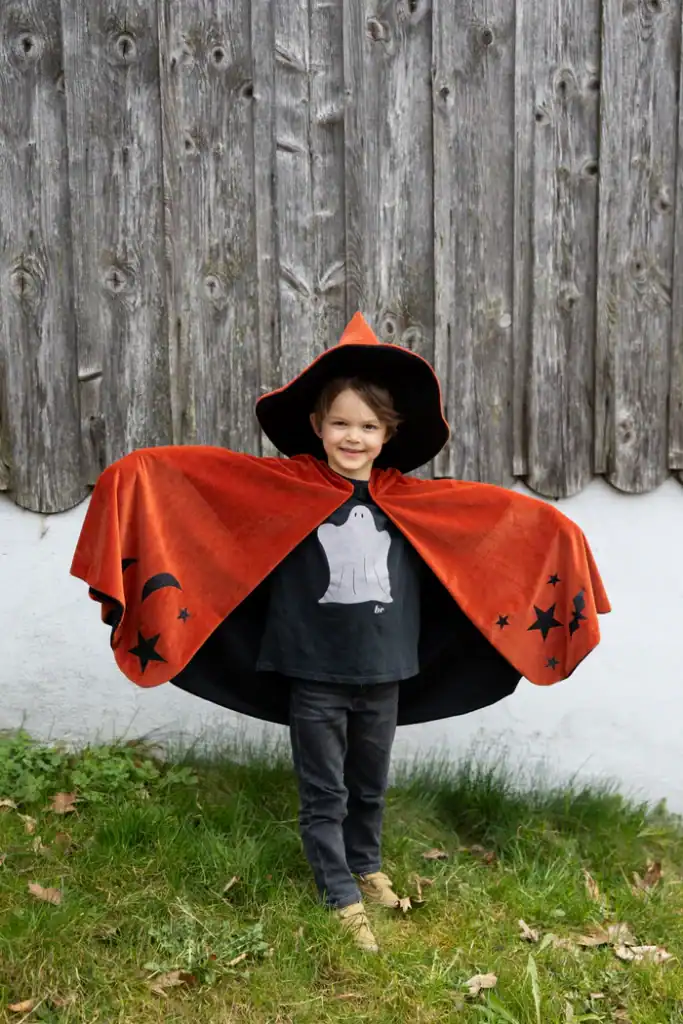 Child wearing witch costume with orange cape