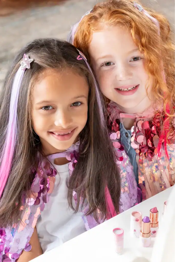 Two children smiling with colorful makeup and capes.