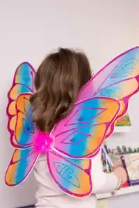 Girl wearing colorful fairy wings reading a book.