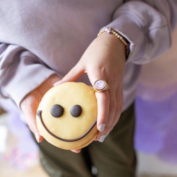 Hands holding a smiley face donut with ring