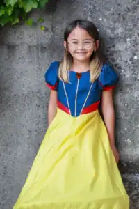 Child in Snow White costume smiling by stone wall