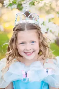 Smiling child wearing a jeweled crown outdoors.