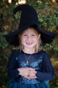 Young girl in witch costume smiling outdoors.