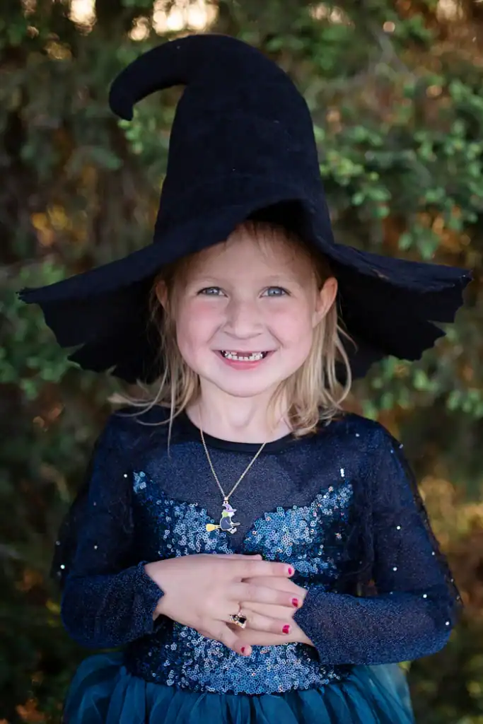 Young girl in witch costume smiling outdoors.