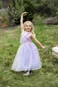 Girl in a purple dress dancing outdoors.