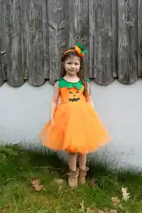 Child in pumpkin costume standing outside.