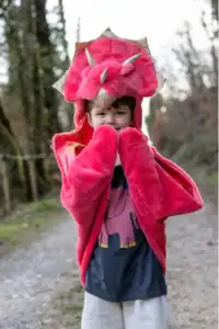 Child in pink dinosaur costume outdoors.