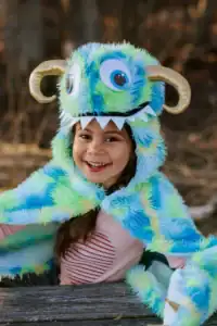 Child smiling in colorful monster costume outdoors.