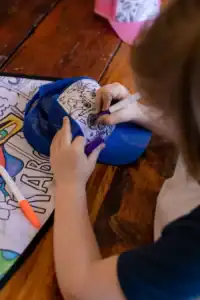 Child coloring a cap with markers.