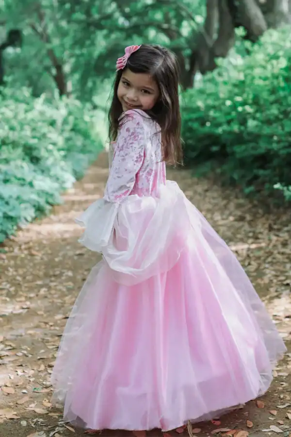Smiling girl in a pink princess dress outdoors.