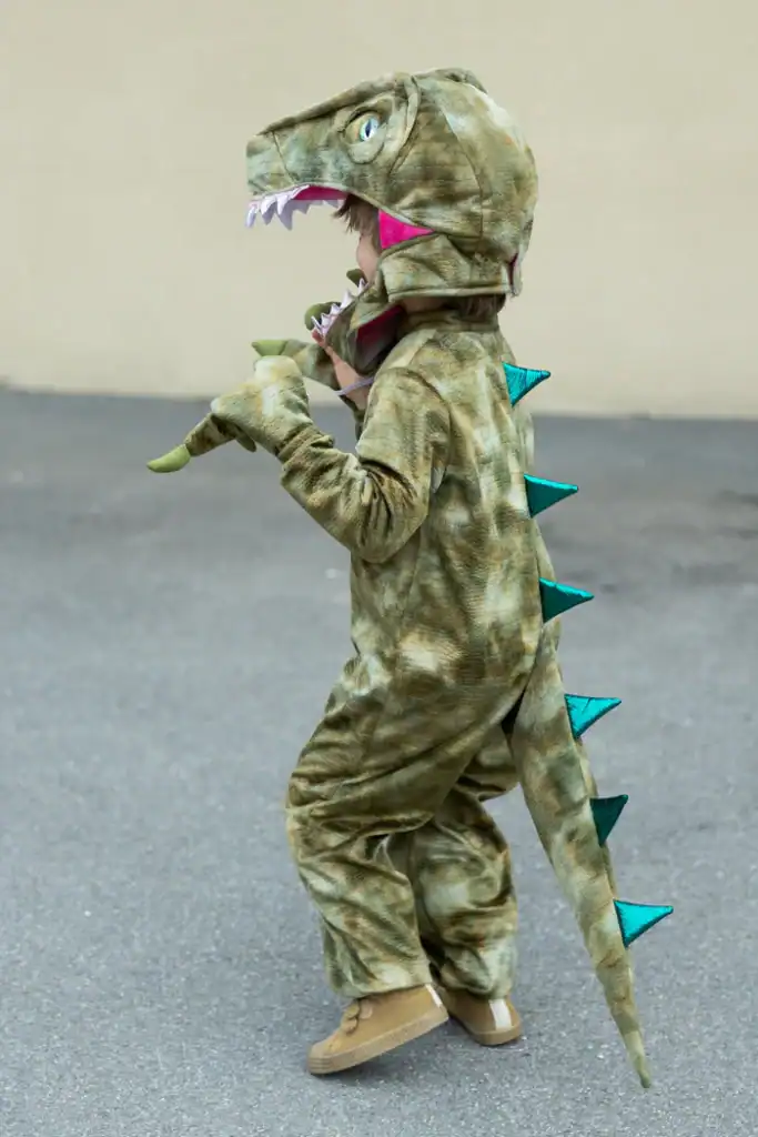 Child wearing dinosaur costume outdoors.
