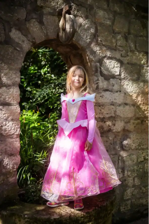 Girl in a pink princess dress by stone archway.