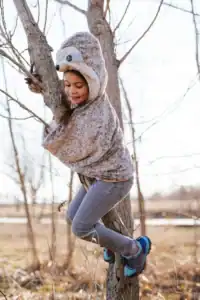 Child climbing tree in sloth hoodie.