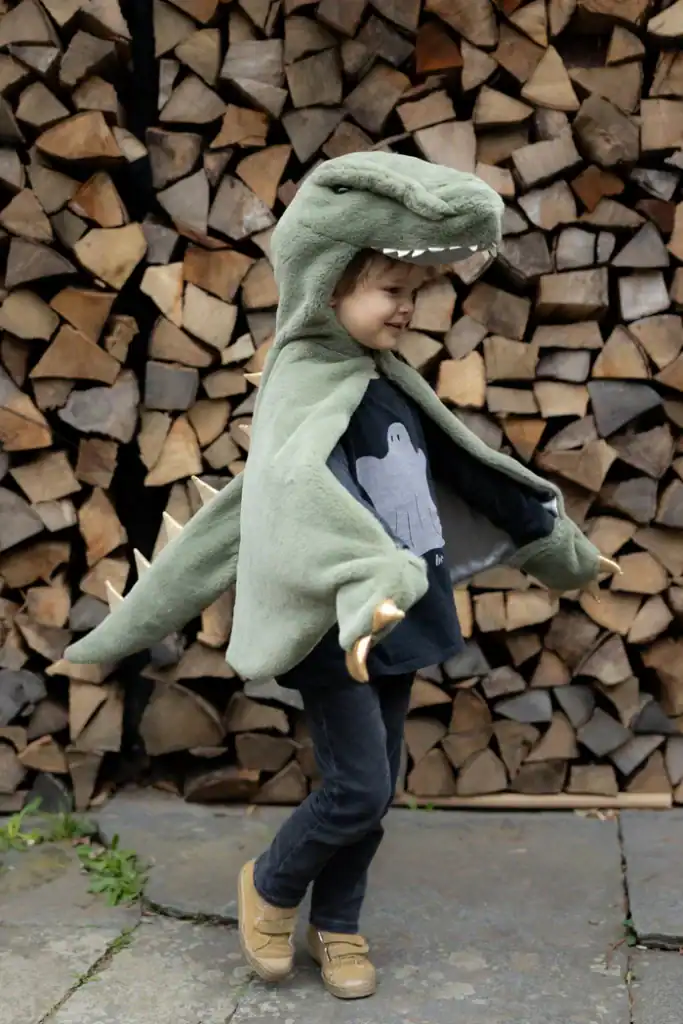 Child wearing dinosaur costume in front of logs.
