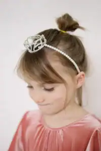 Child wearing crown headband and pink velvet dress.